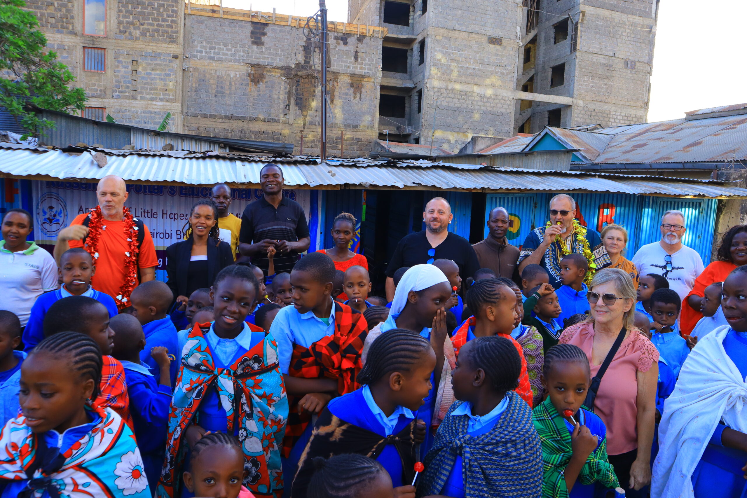 Children and ministry visitors gathered together outside blue buildings in Kenya