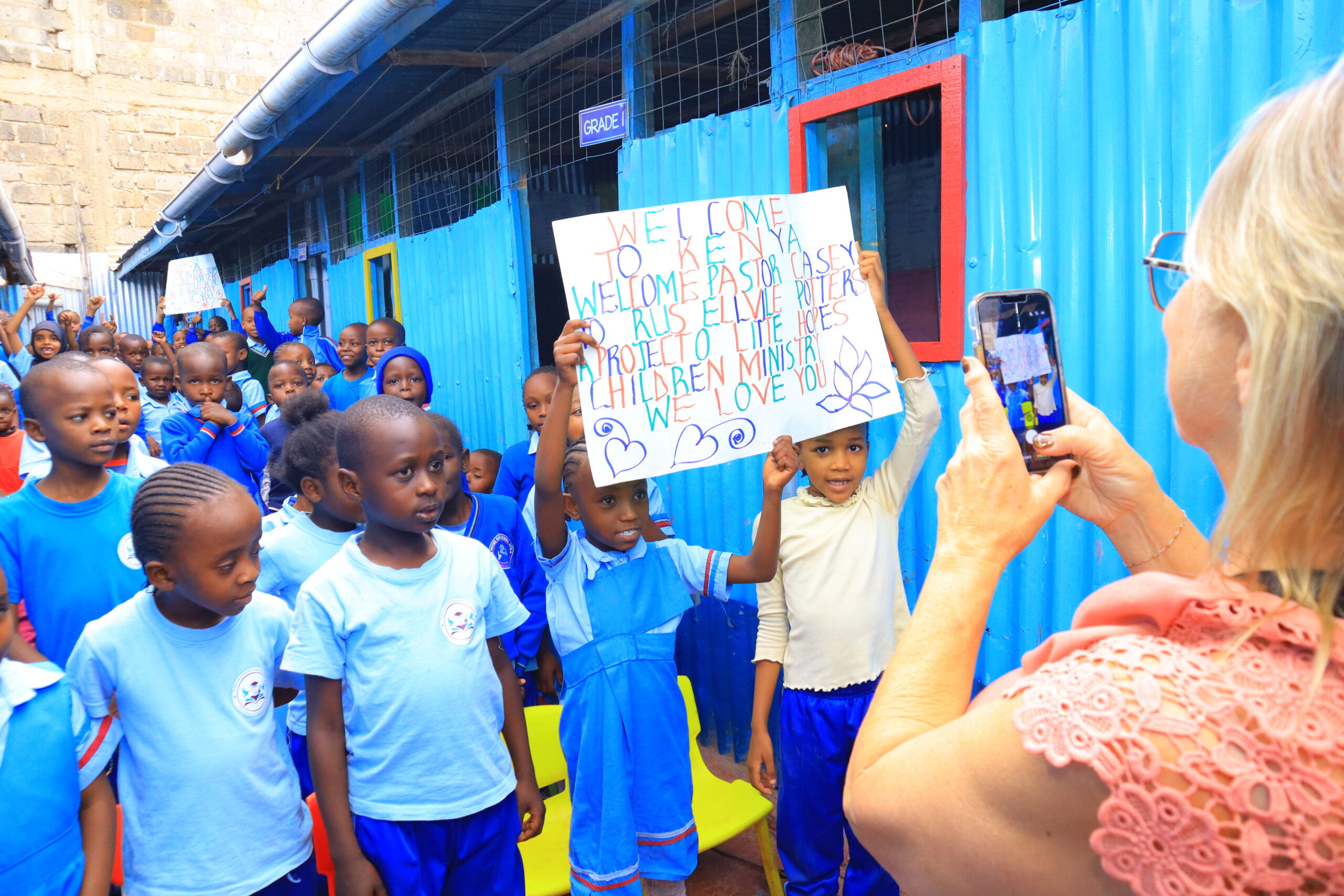 Children in blue school uniforms with handmade welcome signs during a visit in Kenya